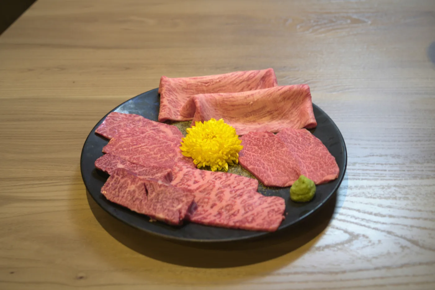 黒い皿に盛りつけた数種類の牛肉と、黄色い花の飾り