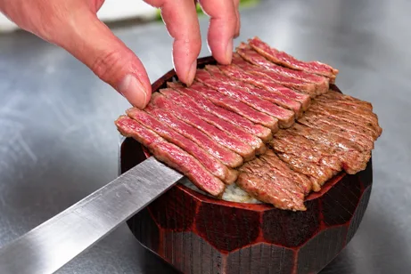 器に盛ったご飯の上の焼いた牛肉を、包丁で切り分ける手元