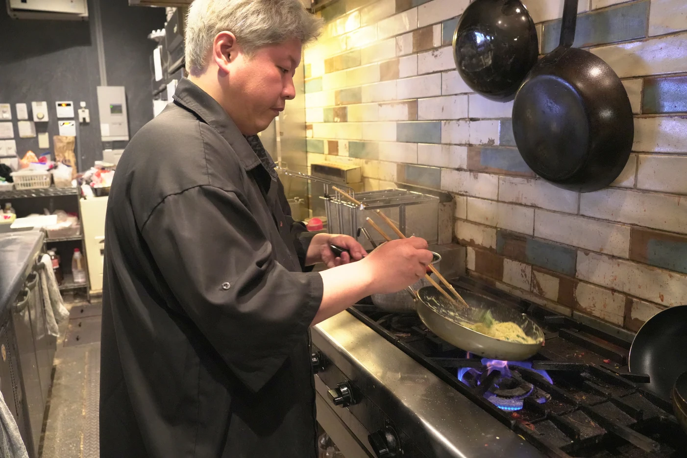 厨房でフライパンを振る店主
